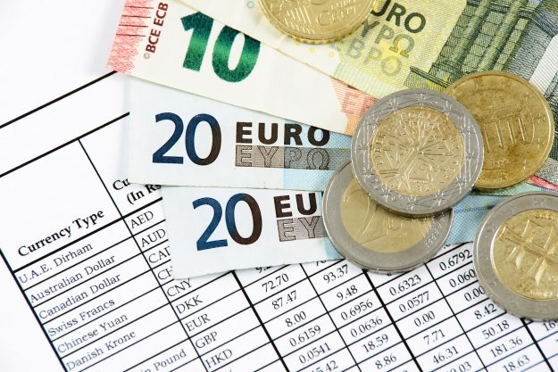 Euro currency notes and coins displayed over a financial report, symbolizing the costs and budgeting involved in M&A transactions.