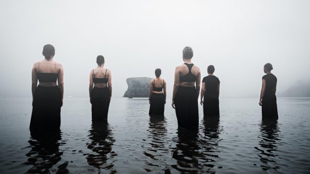 A group of people standing in water, facing uncertainty—symbolizing the disruption caused by the worst 3 things said during M&A integration. Miscommunication can break trust and derail success.