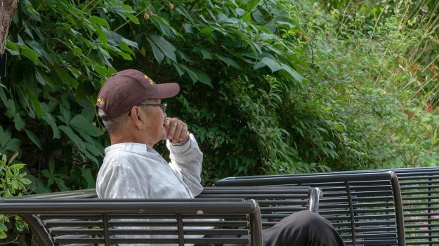 An elderly man in thoughtful posture sits alone on a bench in a quiet, green park—symbolizing reflection and strategic contemplation. This image is used in the article titled “Addressing the Strategic Thinking Crisis in Senior Leaders,” highlighting the importance of deep thinking in leadership