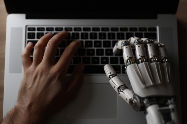 Headcount Is Dead: Why HR Must Embrace Human–AI Workforce Ratio — a human hand and a robotic hand typing together on a laptop, symbolizing the future of blended human–AI workforces.